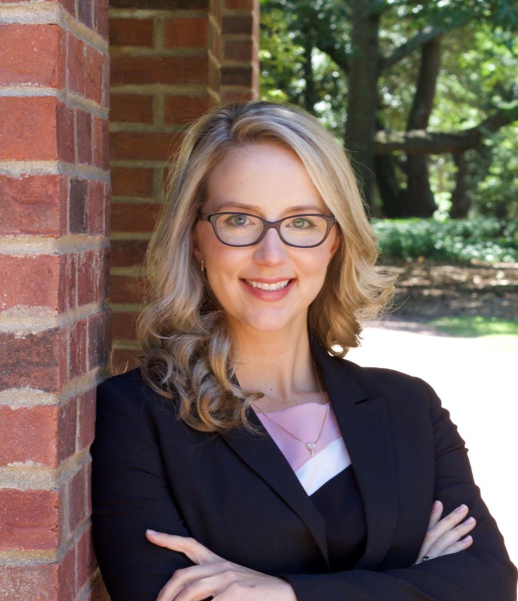 Ms. Marissa Smith, a Caucasian female with long blond hair wears black rimmed glasses and a black suit jacket with a white shirt while smiling at the camera.